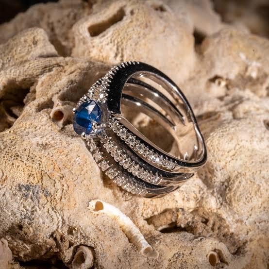 Anillo con una piedra azul y filas de brillantes sobre una roca de coral