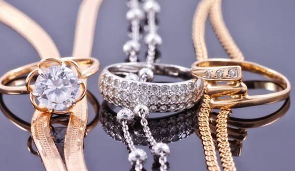 Anillos y cadenas dorados y plateados sobre una superficie reflectante
